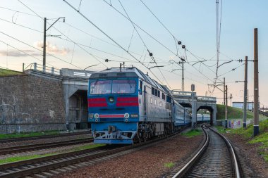 Kharkiv, Ukrayna - 2021 yazı: Truskavets 'e giden şehirlerarası bir yolcu treni taşıyan güçlü dizel lokomotif TEP70 demiryolu kavşağından geçer. Akşam aydınlatması. Ukrayna demiryolları