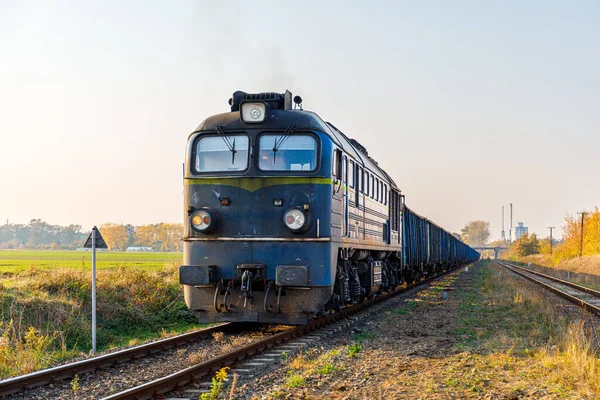 Güçlü bir dizel lokomotif tren istasyonunun rayları boyunca kömür yüklü vagonları çeker. Gün batımı aydınlatma.