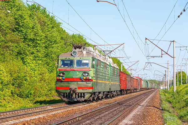 Güçlü yeşil bir elektrikli lokomotif limandaki tren istasyonuna kömür yüklü vagonları çekiyor. Güneşli hava.