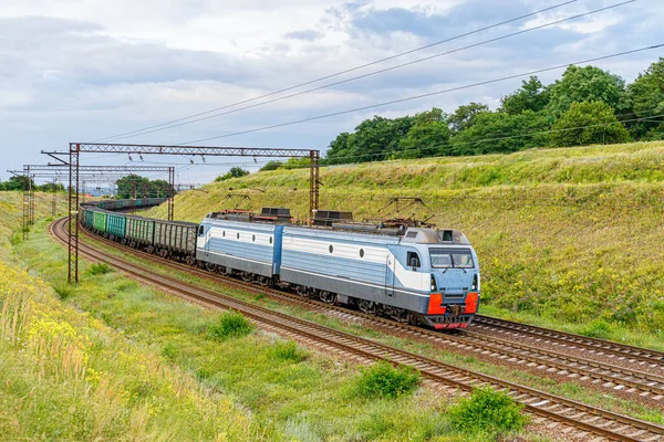 Güçlü gri elektrikli bir lokomotif limandaki tren istasyonuna kömür yüklü vagonları çekiyor. Bahar.