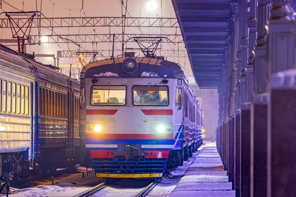 Banliyö yolcusu elektrikli tren merkezi tren istasyonunun platformunda yer almaktadır. Akşam aydınlatması. Kış karlı hava.