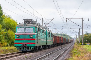 Yeşil bir lokomotif hurda metal yüklü bir treni limandaki tren istasyonuna çeker. Yeşil ve sarı yapraklı ağaçlar. Akşam sonbahar aydınlatması.