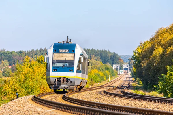 Tek arabalı bir tren otobüsü yerel bir güzergahı takip ederek banliyö tren istasyonuna gider. Sarı yapraklı ağaçlar. Yakın çekim görünümü.