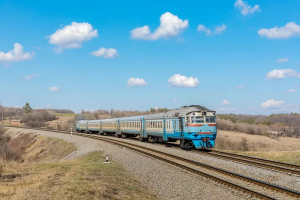 Uzun mavi bir dizel yolcu treni tren rayları boyunca seyahat eder. Bahar güneşli fotoğraf