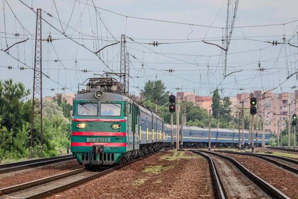 Kharkiv, Ukrayna - Yaz 2021: Uzun bir yolcu treni ile büyük bir tren istasyonu boyunca seyahat eden yeşil bir VL82 elektrikli lokomotif. Yaz akşamı fotoğrafı..