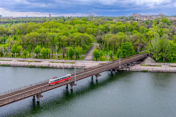 Kryvyi Rih, Ukrayna - 2021 İlkbaharı: Kırmızı bir Tatra T3 tramvayı bir gölet üzerinde bir köprüye biniyor. Yukarıdan görüntüle.