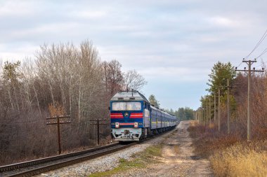 Lisichansk, Ukrayna - sonbahar 2021: Diesel lokomotif TEP70 sonbahar ormanı boyunca demiryolu hattı boyunca uzun bir yolcu treni çekiyor. Ukrayna demiryolları.