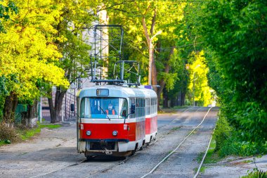 Dnipro, Ukrayna - İlkbahar 2022: Tatra T3 tramvayının yenilenmiş arabaları şehir caddesi boyunca raylarda kırmızı renkli yolculuk yapıyorlar. Yeşil yapraklı ağaçlar. Şehir yolcusu elektrikli taşıma.