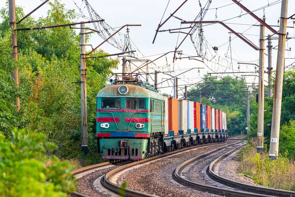 Güçlü bir yeşil lokomotif, konteynırlı vagonları bir gemiye yüklemek için tren istasyonuna çeker. Yakın çekim görünümü.