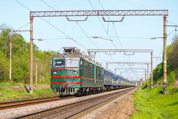 Güçlü iki bölümlü bir lokomotif uzun bir mavi yolcu vagonunu tren istasyonuna çeker. Yolcu demiryolu taşımacılığı. Yakın çekim görüntüsü. Yaz güneşli hava.