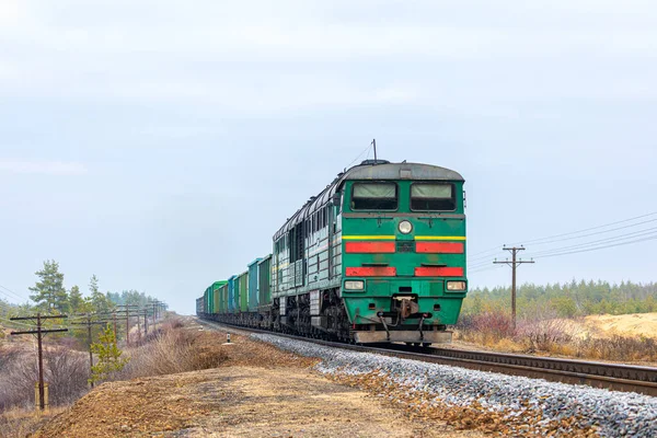 Güçlü yeşil bir lokomotif, bir dağ madeninin tren istasyonuna kömür yüklemek için vagonlardan oluşan uzun bir treni çeker. Kış havası.
