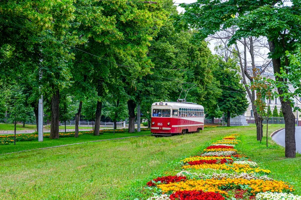 Kharkiv, Ukrayna - İlkbahar 2022: Yolcu tramvayı şehir merkezinde cadde boyunca gidiyor. Yeşil yapraklı ağaçlar ve çiçek tarhları. Şehir yolcusu elektrikli taşıma.