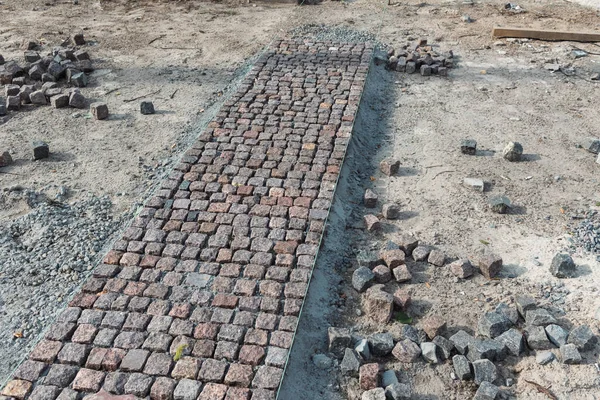 Stone pavement, construction worker laying cobblestone rocks on sand.