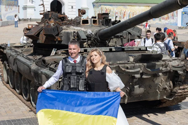 KYIV, UKRAINE - 18 Haziran 2022: Ukraynalı yeni evliler, Ukrayna bayrağını yanmış Rus tanklarının zemininde tutuyorlar. Ukrayna savaşta