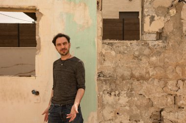 Terk edilmiş ve yıkılmış bir evin boş penceresinin yanında bir adam duruyor.