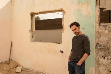 Terk edilmiş ve yıkılmış bir evin boş penceresinin yanında bir adam duruyor.