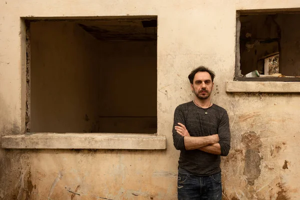 Terk edilmiş ve yıkılmış bir evin boş penceresinin yanında bir adam duruyor.