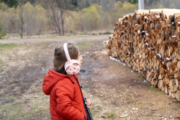 Gadis kecil berjalan di dekat tumpukan kayu bakar — Stok Foto