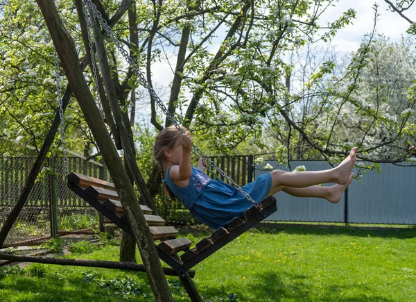 Little girl barefoot rides on a swing on a sunny day — Stok Foto