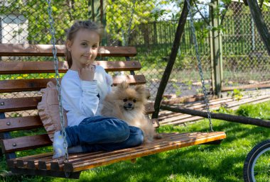 Mutlu küçük kız baharda bir bankta oturur ve küçük köpeğine sarılır. Çocuklar ve Köpekler Dışarıda