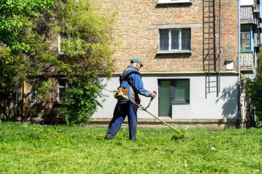 Kasabada elektrikli çim biçme makinesiyle çim biçen bir işçi. Bahçıvanlık malzemeleri ve ekipmanlar. Çim biçme makinesiyle çim biçme işlemi