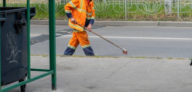 Süpürgeyle caddeyi süpüren adam, elinde çöp için süpürge sapı fırçası olan üniformalı belediye çalışanı, temizlik servisi. Süpürgeli erkek hademe, çöpten şehri temizliyor..