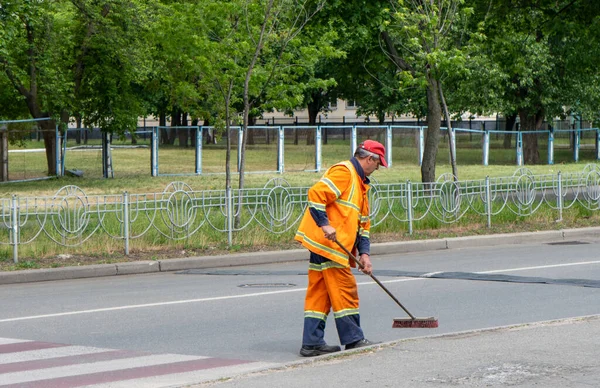 Man cleaner sweeping street with broom, municipal worker in uniform with broomstick brush in hands, cleaning service. Male janitor with broom , cleaning city from garbage near a pedestrian crossing — Stock Photo, Image