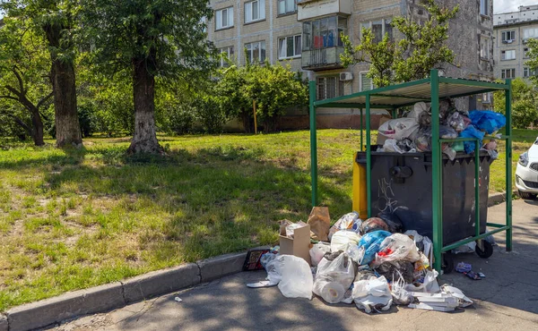 Overflowing garbage can in the city. Huge garbage piles next to the dumpster. Recycling bin overflowing with rubbish on the street. High quality photo