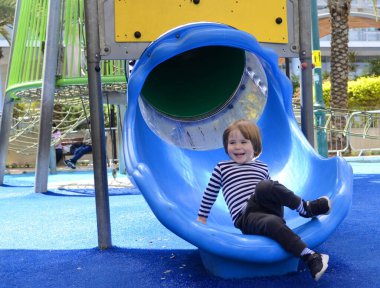 Küçük tatlı bir çocuk kaydırağın üzerinde yuvarlanıyor. Parlak renkli oyun alanı