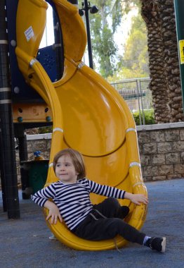 Küçük tatlı bir çocuk kaydırağın üzerinde yuvarlanıyor. Parlak renkli oyun alanı