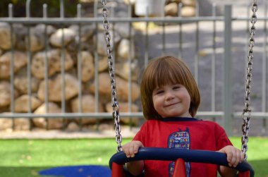 Küçük şirin çocuk parkta salıncakta sallanıyor. Çocuk gülüyor. yakın plan portre