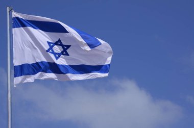 Flag of Israel against a bright blue sky. Star of David on a white background.