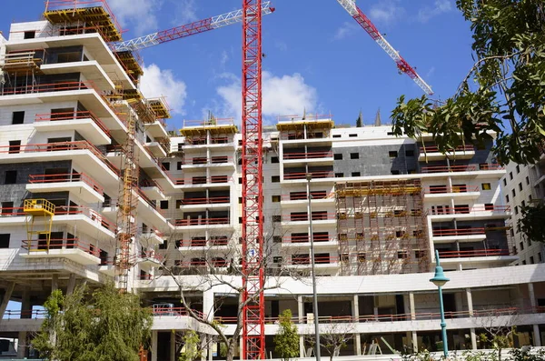 Büyük bina. İnşaat vinci. Etrafta büyük beyaz ev ve palmiye ağaçları var. İsrail 'de İnşaat.