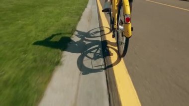 30.05.2021. Kyiv. Ukrayna - Kız sarı bir bisiklet sürüyor. Ayaklar yakın çekimde pedal çeviriyor. Yolda bisiklet gölgesi var. Bisikletli bir anne, pembe motosikletli bir kız.