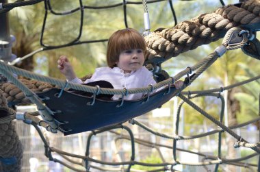 Ağlara tırmanırken tezahürat yapan mutlu şirin çocuk. Çocuk oyun sahasında halat örgüsü üzerinde sürünüyor