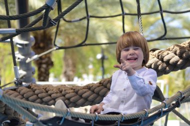 Oyun parkı. Oyun şebekesi. İp parkı. Küçük bir çocuk hamakta oturur ve parmağını gösterir. Çocuk işaret parmağı.
