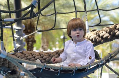 Ağlara tırmanırken tezahürat yapan mutlu şirin çocuk. Çocuk oyun sahasında halat örgüsü üzerinde sürünüyor