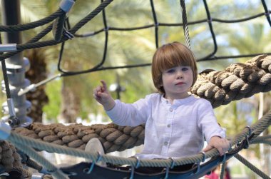 Oyun parkı. Oyun şebekesi. İp parkı. Küçük bir çocuk hamakta oturur ve parmağını gösterir. Çocuk işaret parmağı.