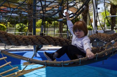 Ağlara tırmanırken tezahürat yapan mutlu şirin çocuk. Çocuk oyun sahasında ip örgüsü üzerinde sürünüyor. Beyaz gömlekli şirin bir çocuk hamakta yatıyor. Oyun parkında şebeke, ip parkı. Faaliyetler için internet. Çocuk dinleniyor.