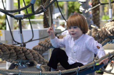 Oyun parkı. Oyun şebekesi. İp parkı. Küçük bir çocuk hamakta oturur ve parmağını gösterir. Çocuk işaret parmağı.