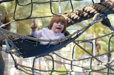 Oyun parkı. Oyun şebekesi. İp parkı. Küçük bir çocuk hamakta oturur ve parmağını gösterir. Çocuk işaret parmağı.