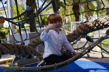 Oyun parkı. Oyun şebekesi. İp parkı. Küçük bir çocuk hamakta oturur ve parmağını gösterir. Çocuk işaret parmağı.