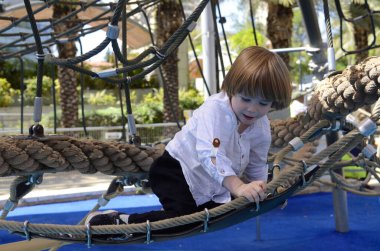 Ağlara tırmanırken tezahürat yapan mutlu şirin çocuk. Çocuk oyun sahasında ip örgüsü üzerinde sürünüyor. Beyaz gömlekli şirin bir çocuk hamakta yatıyor. Oyun parkında şebeke, ip parkı. Faaliyetler için internet. Çocuk dinleniyor.