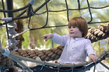 Oyun parkı. Oyun şebekesi. İp parkı. Küçük bir çocuk hamakta oturur ve parmağını gösterir. Çocuk işaret parmağı.