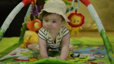 6 month old boy wearing a safari hat on a jungle play mat. Cute baby laughs, plays on the mat. The boy smiles at the camera.