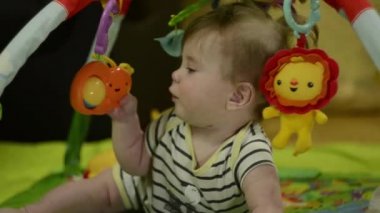 Küçük bir çocuk kameraya bakıyor. Sırtüstü uzanıyor ve hareketli ve yumuşak oyuncaklarla oynuyor. Çok ciddi görünüyorsun.