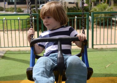 Küçük mutlu çocuk dışarıda salıncakta eğleniyor. Parkta salıncakta sallanan pozitif çocuk eğleniyor. Mutlu çocuk sallanmaktan zevk alır. Sevimli bir anaokulu çocuğu portresi.