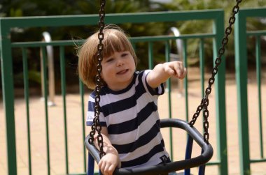 Küçük mutlu çocuk dışarıda salıncakta eğleniyor. Parkta salıncakta sallanan pozitif çocuk eğleniyor. Mutlu çocuk sallanmaktan zevk alır. Sevimli bir anaokulu çocuğu portresi.