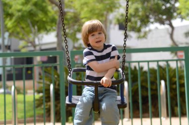 Küçük mutlu çocuk dışarıda salıncakta eğleniyor. Parkta salıncakta sallanan pozitif çocuk eğleniyor. Mutlu çocuk sallanmaktan zevk alır. Sevimli bir anaokulu çocuğu portresi.