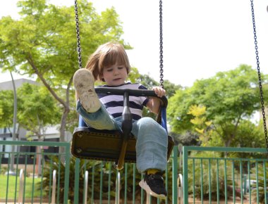 Küçük mutlu çocuk dışarıda salıncakta eğleniyor. Parkta salıncakta sallanan pozitif çocuk eğleniyor. Mutlu çocuk sallanmaktan zevk alır. Sevimli bir anaokulu çocuğu portresi.